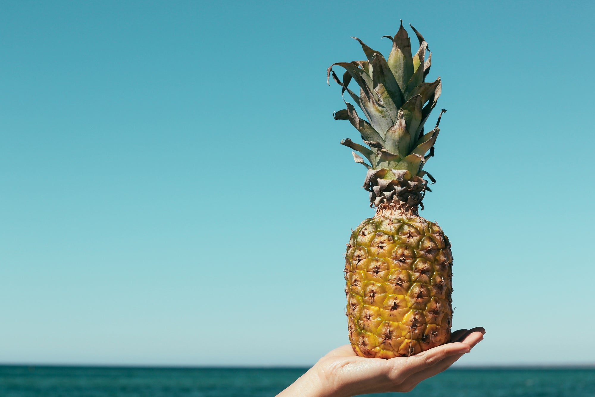 Ananas auf einer Hand vor dem Meer in die Luft gehoben.